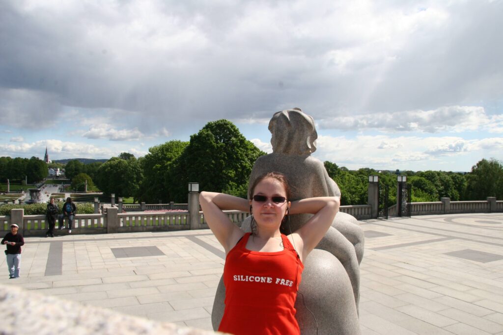 Woman leaning on a statue in a park in Norway, wearing a red top